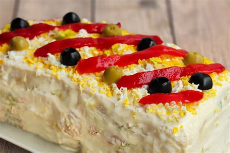 Fotografía de un pastel sándwich decorado con aceitunas, huevo rallado y tiras de pimiento