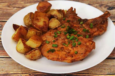 Plato terminado de chuletas de cerdo al horno con patatas y zanahorias asadas.