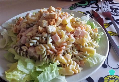 Imagen de una ensalada de pasta con piña, jamón y maíz, servida sobre una cama de lechuga y decorada con picatostes.