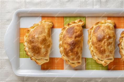 Foto de varias empanadas horneadas de diferentes formas y tamaños en una bandeja, algunas cortadas para mostrar el relleno