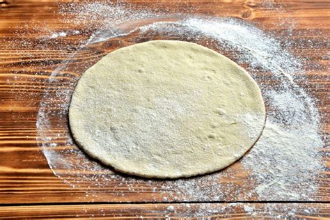 Masa de pizza estirada en forma circular sobre una superficie enharinada.