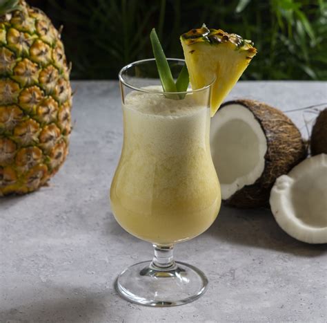 Foto profesional de una Piña Colada servida en un vaso tipo huracán con decoración de piña y sombrilla