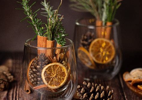 centro de mesa aromático con piñas, ramas de canela, romero y rodajas de naranja deshidratada en un recipiente de cristal
