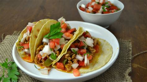 Composición de tacos listos para servir, mostrando el relleno, queso, pico de gallo y un gajo de limón.