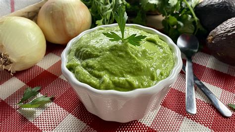 Fotografía apetitosa de un bol con guasacaca fresca y vibrante, rodeado de cilantro y aguacate.