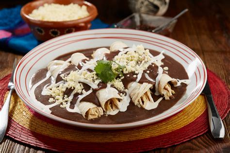 Plato servido de enfrijoladas con pollo adornado con queso, crema y cilantro fresco.