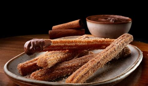 Primer plano de unos churros crujientes espolvoreados con azúcar y canela, junto a una taza de chocolate caliente.