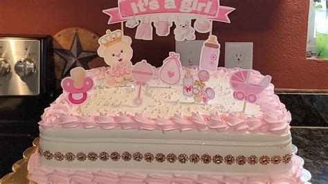 Un pastel de baby shower de niña con un osito de fondant rosado como figura principal, rodeado de esferas de fondant y detalles en color pastel.