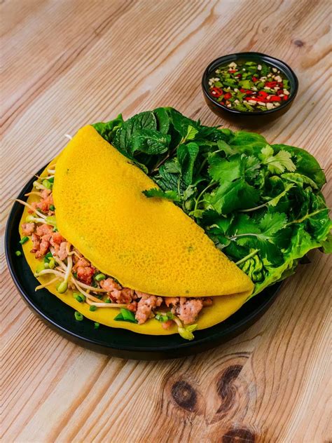 Imagen de un Banh Xeo recién hecho, con sus ingredientes visibles y una porción lista para ser envuelta en lechuga
