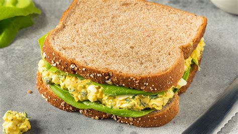 Fotografía de un sándwich gourmet servido en pan de campo con aceitunas y huevo duro.