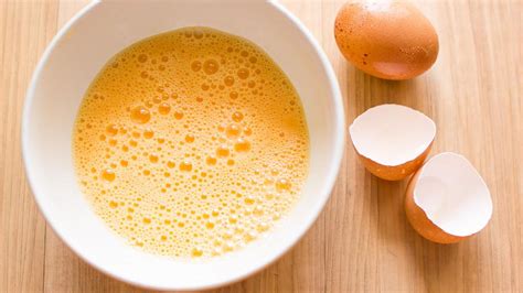 Primer plano de huevos y azúcar siendo batidos hasta obtener una mezcla cremosa y clara.