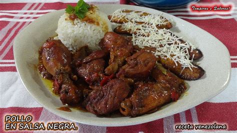 Plato de pollo en salsa negra servido con arroz blanco y plátanos maduros fritos.