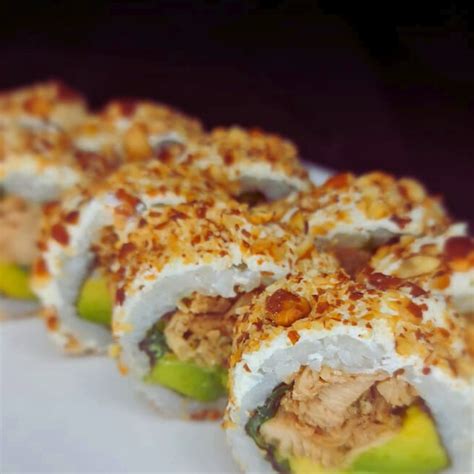 Fotografía de primer plano de un roll cubierto con palta y topping de camote crocante con salsa acevichada.