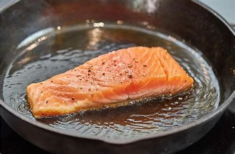 Filetes de salmón sellándose en un sartén con mantequilla y limón