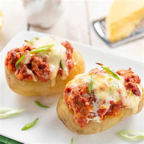 Primer plano de papas rellenas listas para hornear con espinaca y queso gratinado.