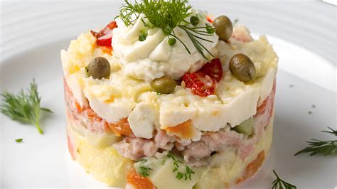 Plato de ensaladilla rusa tradicional ricamente decorada con atún, huevo y pimiento rojo.