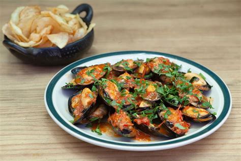Foto de choritos caldosos con tomate y ajo, servidos en un plato hondo
