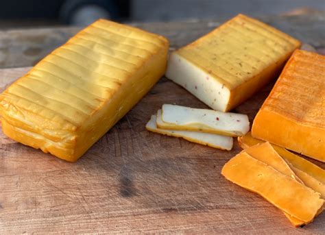 Composición de queso ahumado artesanal sobre una tabla de madera, acompañado de uvas y frutos secos.