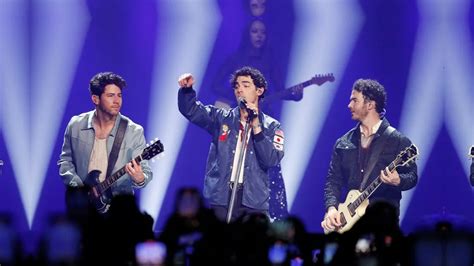 Fotografía de los Jonas Brothers actuando en la serie, con instrumentos musicales y un fondo de escenario