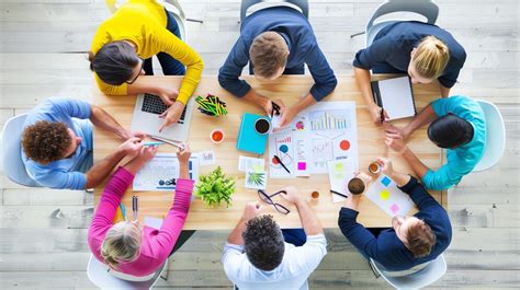 Esquema visual del reto: un grupo trabajando en una mesa con espaguetis, cinta y un malvavisco en la cima de una estructura de celosía triangular.