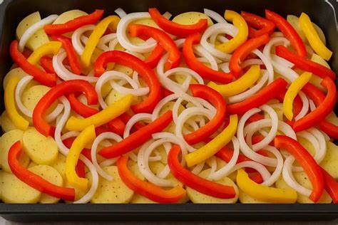 Fotografía de bandeja de horno con cama de patatas, pimientos y longanizas dorándose