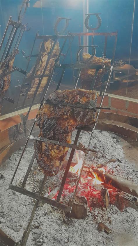 Fotografía de un asado cocinándose dentro de una estructura en forma de jaula sobre brasas.