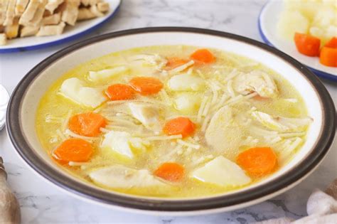 Un tazón humeante de sopa de pollo y arroz con trozos de pollo y verduras
