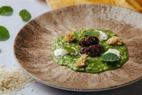 Fotografía de un risotto vibrante de color verde, servido con trozos de queso.
