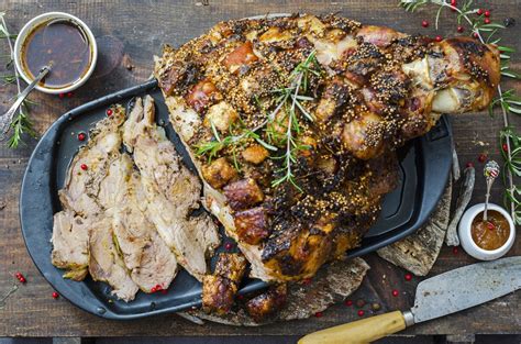 Imagen de una paleta de cerdo asada servida en una fuente, con rodajas de carne jugosa y salsa alrededor.