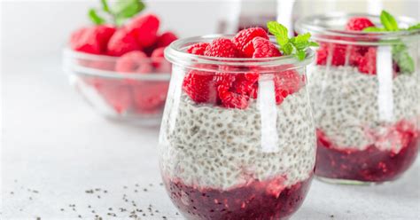 Fotografía de diferentes capas de yogurt con chía, frutas rojas y semillas presentadas en frascos de vidrio