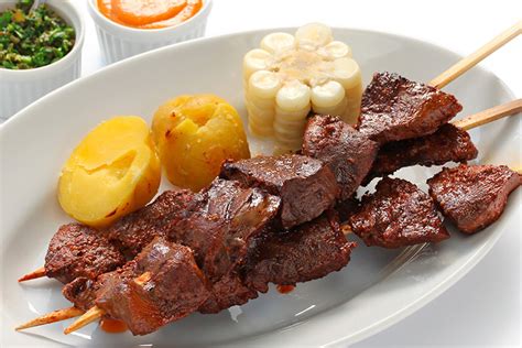 Anticuchos peruanos con corazón de vaca, patatas y salsa criolla en un plato
