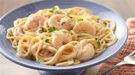 Plato de pasta fettuccine con camarones rosados en salsa cremosa Alfredo, decorado con perejil fresco picado
