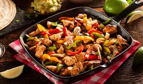 Plato de fajitas con los ingredientes separados: tiras de carne, pimientos, cebolla, tortillas y salsas.