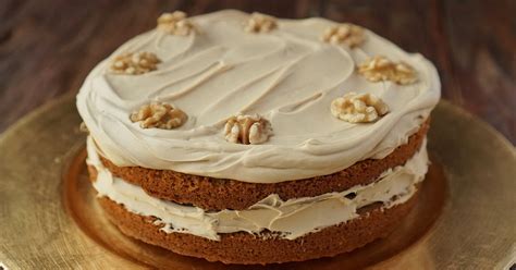 Fotografía de una tarta de café y nueces en capas, decorada con nueces enteras y frutos rojos sobre un plato elegante.