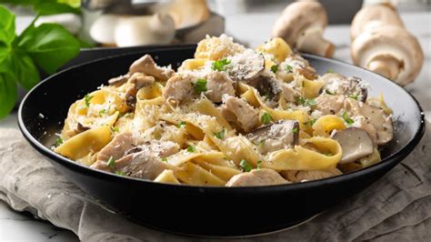 Plato principal de pasta cremosa con jamón y champiñones, servido en un plato blanco con perejil picado por encima