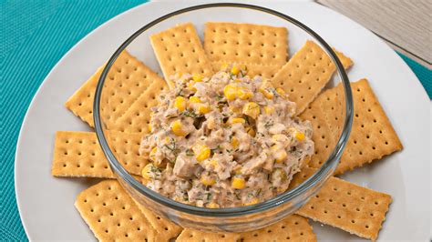 Imagen de un cuenco con dip de atún cremoso decorado con cebollino fresco, acompañado de tostadas y vegetales.