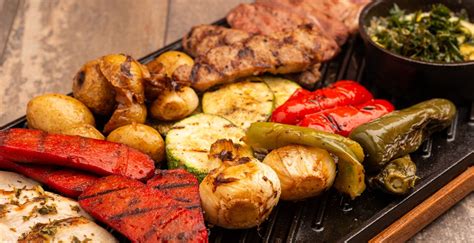 Fotografía de una parrillada variada y apetitosa, con diferentes tipos de carne a la brasa, acompañada de guarniciones frescas.