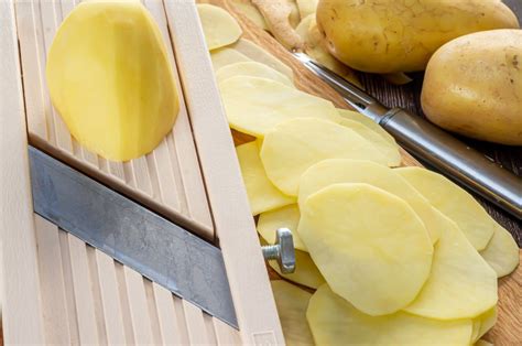 Primer plano de papas siendo cortadas en rodajas finas con una mandolina.