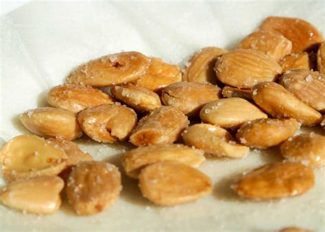 Plato de almendras fritas saladas con una bebida fría en el fondo