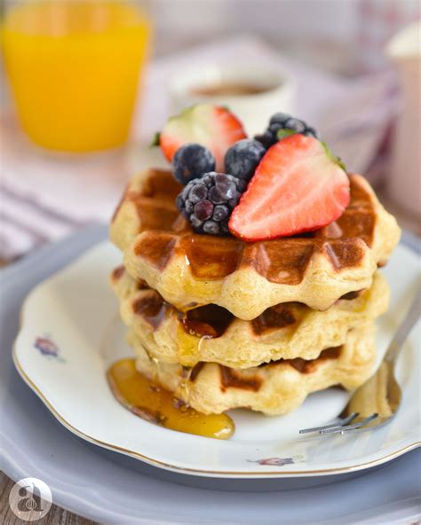 Fotografía profesional de waffles belgas recién hechos, dorados y crujientes, con azúcar glass y frutos rojos frescos encima.