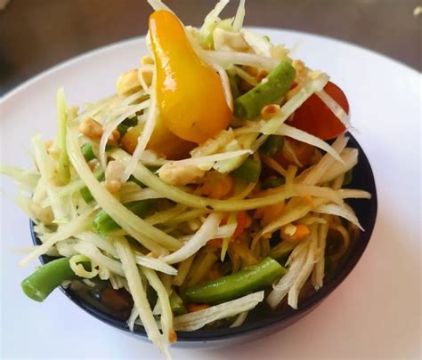 Ensalada de papaya verde con maní, chiles y pollo asado en un cuenco de madera