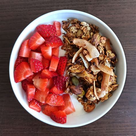 Un bol de yogur griego con fresas, arándanos, granola y miel, presentado de forma atractiva