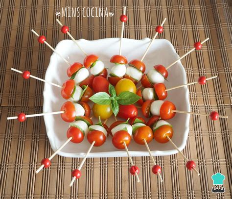Varias brochetas de tomate cherry y queso en un plato, con diferentes salsas de acompañamiento