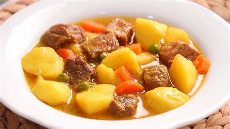 Estofado de vacuno con patatas humeante en un plato, con trozos de carne y patatas visibles, y un trozo de pan.