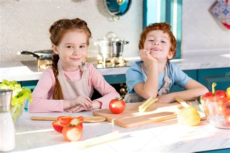 Niños sonriendo mientras cocinan verduras frescas en una cocina luminosa