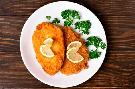 Plato de pechuga apanada servido con acompañamientos frescos y coloridos en una mesa elegante