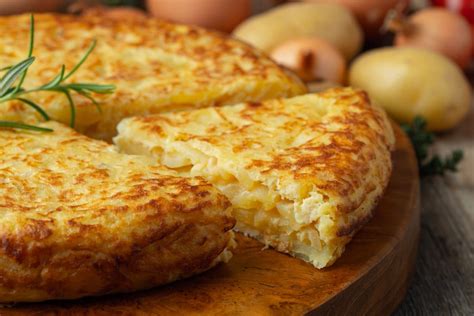 Tortilla de papa dorada y cremosa servida en un plato, con textura fundida de queso y una guarnición de ensalada fresca.