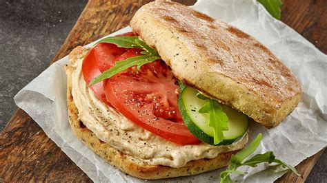 Foto: Presentación de sándwich vegetariano con hummus y vegetales frescos coloridos.