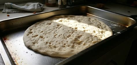 Esquema de una bandeja de horno rectangular con masa de pizza estirada cubriendo toda la superficie para un horneado uniforme.