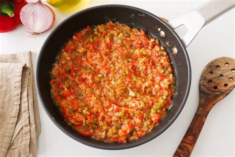 Detalle de un sofrito de cebolla, ajo y pimiento en una cazuela, con aceite de oliva burbujeando.